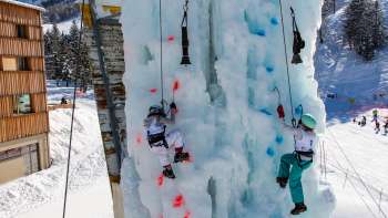 Due bambini che si arrampicano sul ghiaccio sulla torre di arrampicata ghiacciata di Malbun con piccozze e caschetti