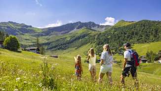 Una famiglia passeggia in un prato estivo in fiore a Malbun, nel Liechtenstein, e si gode la vista delle Alpi circostanti.