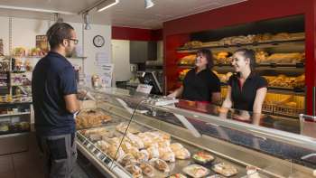 Sala vendite di una panetteria con personale gentile, pane e dolci appena sfornati in primo piano