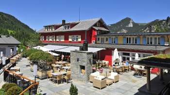 Vista esterna del ristorante alla luce del sole, con facciata rossa e panorama montuoso.