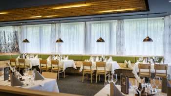 Un'invitante zona pranzo con tavoli rotondi e morbide sedie verdi, arredata in stile moderno e naturale.