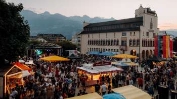 Il Municipio di Vaduz all'imbrunire con luci fiabesche, bambini che giocano su un tavolo da ping pong e un'atmosfera estiva nei giorni festivi