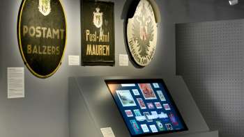 Sala del museo con vecchie insegne postali e un'esposizione digitale sulla storia dell'ufficio postale nel Liechtenstein.