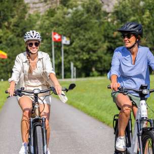 Due donne in e-bike durante un tour estivo con le bandiere del Liechtenstein, della Svizzera e dell'Austria sullo sfondo
