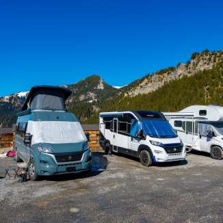 Diversi camper e motorhome in una piazzola tra le montagne del Liechtenstein, sotto un cielo blu brillante