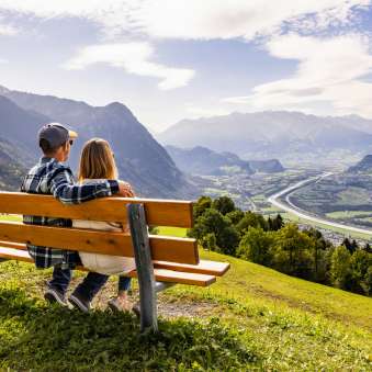 Coppia seduta su una panchina a Triesenberg e affacciata sulla valle del Reno in Liechtenstein con un impressionante panorama alpino