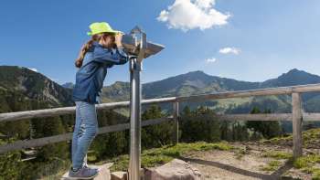 Ragazza con cappello verde guarda attraverso un telescopio sul Sentiero degli esploratori di Malbun con vista panoramica sulle Alpi del Liechtenstein.