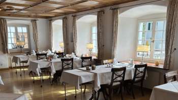 Sala da pranzo luminosa e classica con tovaglie bianche e pavimento in legno.