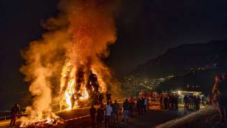 Grande falò notturno nel Liechtenstein, la gente osserva il fuoco ardente su una collina con vista sulla città illuminata e sulle montagne.