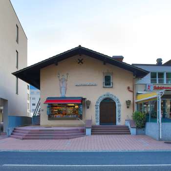 Vista esterna del vecchio cinema di Vaduz con le scritte sopra l'ingresso e le tende da sole rosse, situato tra due edifici moderni.