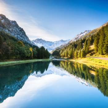 Lago Gänglesee a Steg con riflesso di montagna, circondato da boschi, raggi di sole sul pendio.