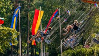 Bambini e adulti salgono su una giostra a catena sotto il sole della fiera di Balzers, circondati da bandiere colorate.