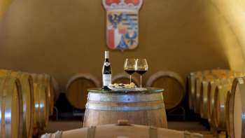 Suggestiva degustazione di vini nella cantina della Cantina Principesca con due bicchieri e una bottiglia di vino rosso su una botte di legno.