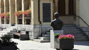 Vista dell'area d'ingresso del Municipio di Vaduz con composizioni floreali, busto storico e ampi gradini in pietra: un punto di riferimento culturale nel centro di Vaduz.
