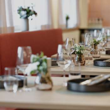 Primo piano dei tavoli elegantemente apparecchiati del ristorante RUUF con stoviglie scure e vasi di fiori