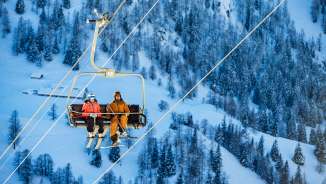 Tina Weirather e Marco Büchel siedono insieme su una seggiovia, circondati da alberi innevati e paesaggi invernali a Malbun.