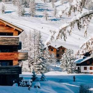 Accoglienti chalet nella località di sport invernali di Malbun circondati da alberi innevati e piste da sci sullo sfondo