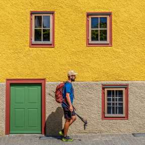 Escursionisti davanti alla Landweibel-Huus di Schaan, con la sua facciata gialla, la porta verde e le cornici rosse delle finestre: un'attrazione del «Sentiero del Liechtenstein».