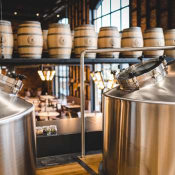 Vista di un moderno birrificio con serbatoi in acciaio inox scintillanti e botti di legno impilate sullo sfondo.