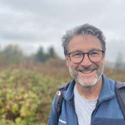 Ritratto di Nikolaus Büchel, guida escursionistica del Liechtenstein, sorridente davanti a un paesaggio autunnale con zaino e giacca da outdoor.