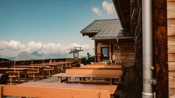 Panche di legno vuote sulla terrazza panoramica del rifugio Sareis con vista sulle Alpi, ideali per una pausa durante un'escursione o un giro sulla ferrovia di montagna.