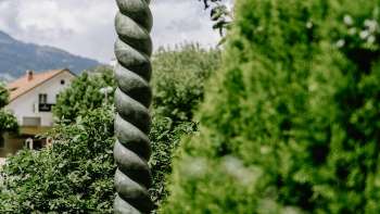 Opera d'arte rinascimentale di Daniel Spoerri, con una suggestiva forma a colonna e una figura in bronzo, immersa nella natura del Liechtenstein.