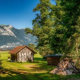 Piccolo fienile in legno su un prato con una catasta di legna da ardere e vista sulle Alpi lungo la Route 66 in Liechtenstein