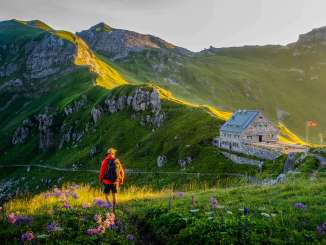 Un escursionista guarda il rifugio Pfälzerhütte nel Liechtenstein, circondato da un verde paesaggio montano e da un panorama alpino nella luce della sera