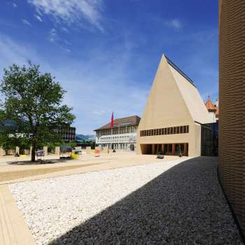 Vista della Peter-Kaiser-Platz, pavimentata in modo luminoso, di fronte all'edificio del Parlamento di Vaduz, con il suo moderno insieme architettonico.