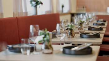 Primo piano dei tavoli elegantemente apparecchiati del ristorante RUUF con stoviglie scure e vasi di fiori