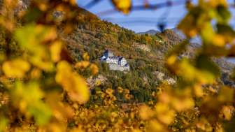 Vista del castello di Vaduz nel Liechtenstein in autunno, incorniciato da foglie giallo oro e da uno sfondo naturale autunnale.