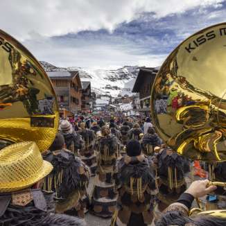 Veduta di un gruppo di Guggenmusik con strumenti dorati alla sfilata di carnevale di Malbun sullo sfondo di una montagna innevata.