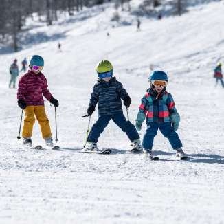 Tre bambini imparano a sciare nell'area sciistica per famiglie di Malbun, in Liechtenstein, sotto il sole e la neve polverosa