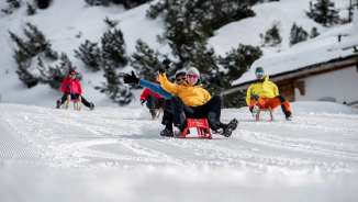 Divertimento in slitta a Malbun Gruppo di felici slittinisti su una pista battuta a Malbun, circondati da alberi innevati e da un paesaggio invernale alpino