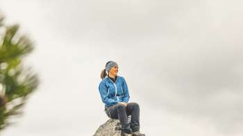 Rosaria Michaela Ackermann si siede su una roccia tra le montagne del Liechtenstein e guarda in lontananza
