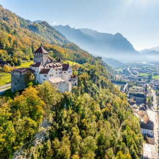 Vista del castello di Vaduz nel Liechtenstein con i colori autunnali, le montagne e la valle del Reno sullo sfondo