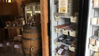 Assortimento regionale nel negozio del maso Hedihof - frigorifero con prodotti di carne confezionati e sala vendita rustica.