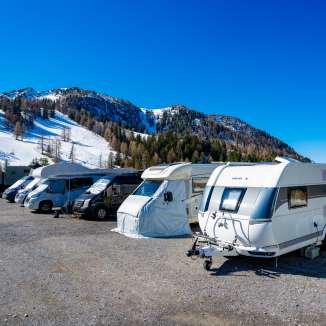 Camper e roulotte parcheggiati in una piazzola innevata a Malbun con vista sulle Alpi