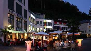 Atmosfera serale davanti alla Brasserie Burg di Vaduz con terrazza illuminata e ospiti sotto gli ombrelloni.