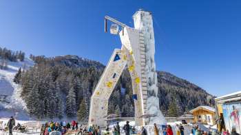 La torre di ghiaccio di Malbun sotto un cielo azzurro, circondata da alberi innevati e sciatori