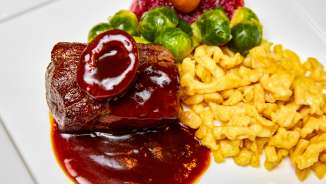 Delizioso piatto di selvaggina con salsa scura, spaetzle giallo oro, cavolini di Bruxelles e mirtilli rossi servito su un piatto bianco.