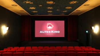 Sala cinematografica del vecchio cinema di Vaduz con poltrone rosse, palco con sipario rosso e soffitto blu con motivi di stelle dorate.