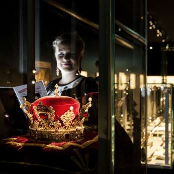 Donna che osserva il cappello principesco nella Camera del Tesoro del Liechtenstein, circondato da vetrine illuminate.