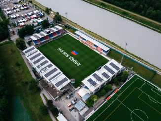 Veduta aerea dello stadio Rheinpark di Vaduz con la scritta "Hoi aus Vaduz" sul campo da gioco e il Reno sullo sfondo