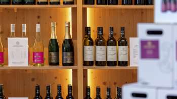 Interno della Hofkellerei con scaffali in legno elegantemente illuminati pieni di bottiglie e cartoni di vino.