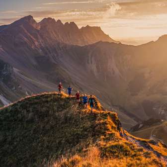 Gruppo di trail runner su una cresta di montagna vicino a Malbun, Liechtenstein, nella calda luce del tramonto con vista sulle Alpi