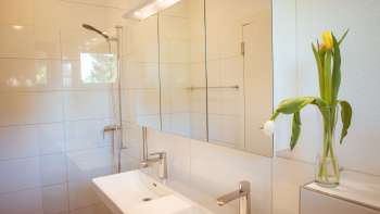 Bagno moderno e luminoso nella guest house del Camping Mittagsspitze con doppio lavabo, specchio e fiori freschi.