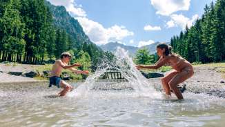 I bambini sguazzano nel lago Gänglesee, vicino a Steg, circondato da boschi e montagne - vivete la natura e rinfrescatevi in Liechtenstein