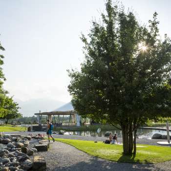 Sentiero soleggiato con alberi ombrosi e vista sull'acqua nell'Impianto ricreativo di Grossabünt a Ruggell.
