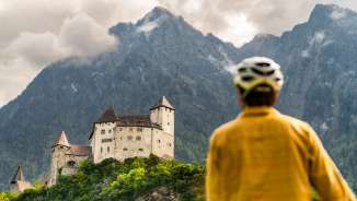 Un ciclista con il casco osserva l'imponente rocca di Gutenberg sullo sfondo delle montagne di Balzers - tour culturale in bicicletta nel Liechtenstein
